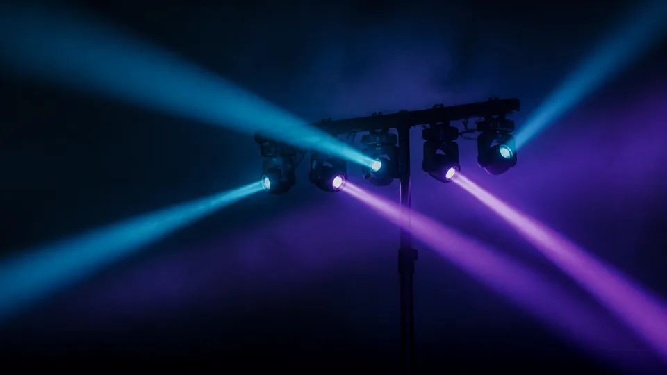 Atmospheric concept image of coloured stage beams cutting through haze above a small stage.
